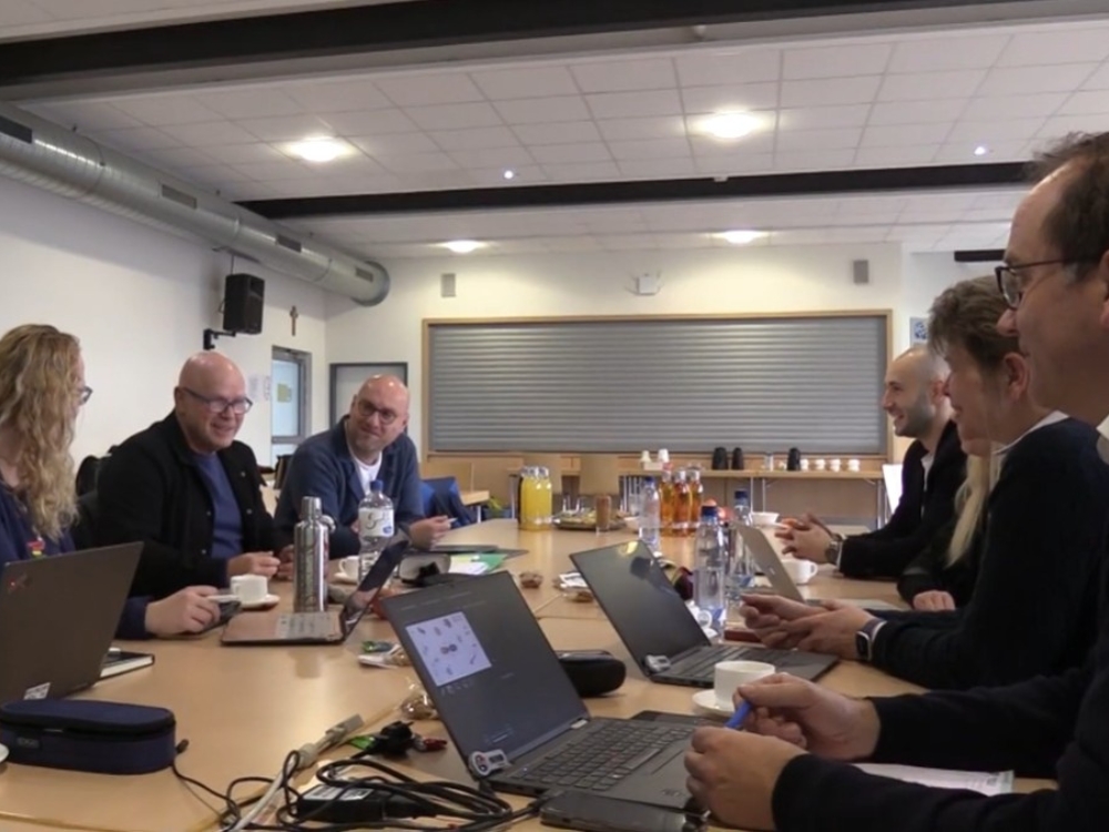 Eine Gruppe von Menschen sitzt mit Laptops an einem Tisch und tauscht sich aus